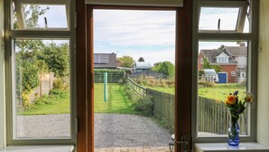 A doorway leading to a paved area with a view of a residential neighborhood and a fence. - Decca Cottage Nidd Grange (York)