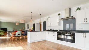 Une cuisine moderne avec des meubles blancs, un four noir et un coin repas comprenant une table et des chaises en bois.