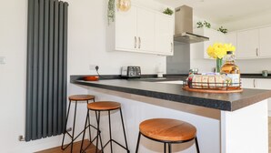 Une cuisine moderne avec un îlot central, des tabourets de bar, un luminaire suspendu et une plante.