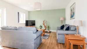 Un salon moderne avec deux canapés gris, une table basse en bois, un téléviseur posé sur un meuble et un luminaire suspendu.