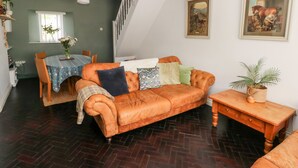 Een gezellige woonkamer met een leren bank, een eettafel met stoelen, een trap en een schilderij aan de muur.