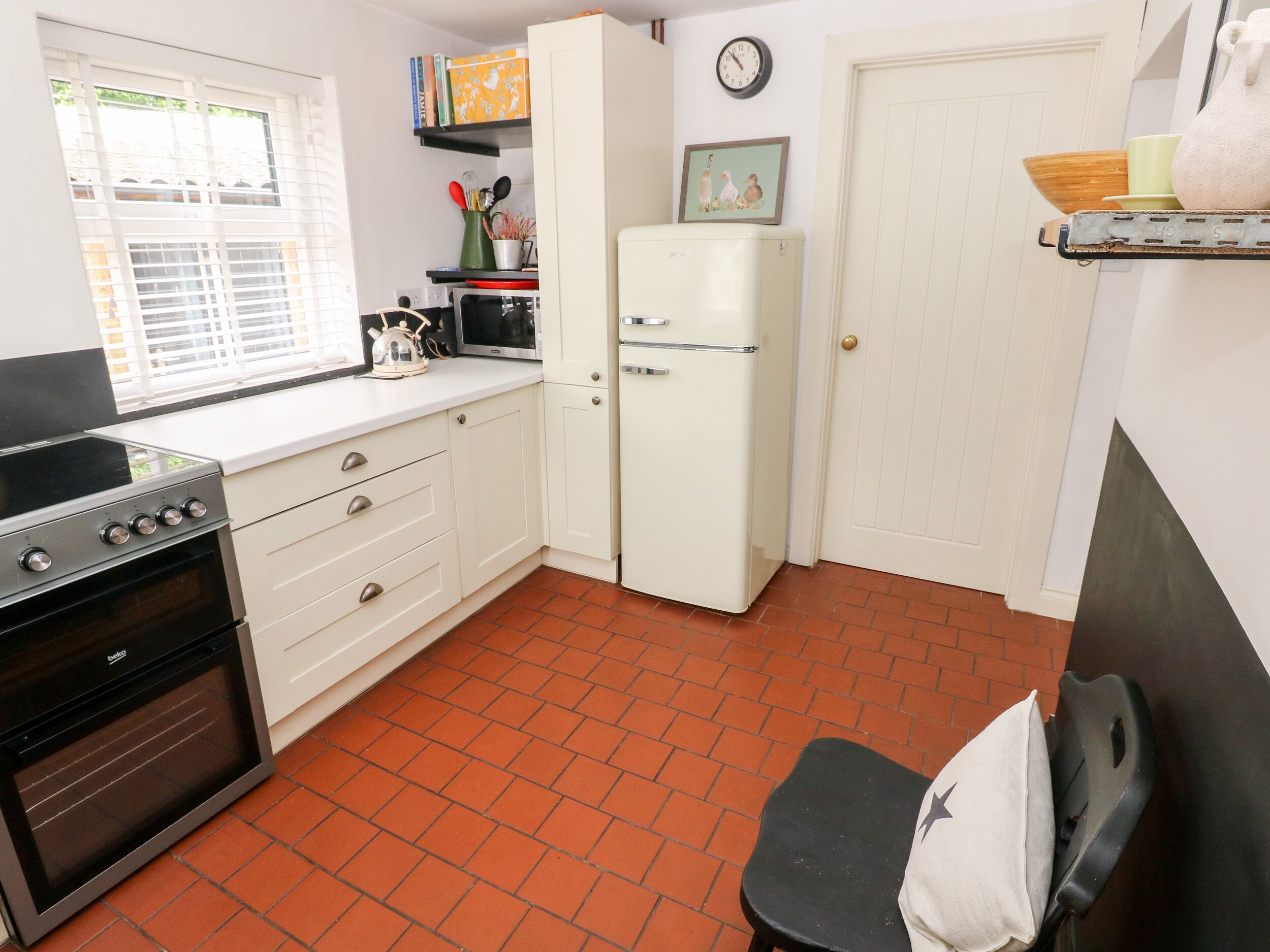 A compact kitchen with a stove, oven, refrigerator, and a window with blinds.