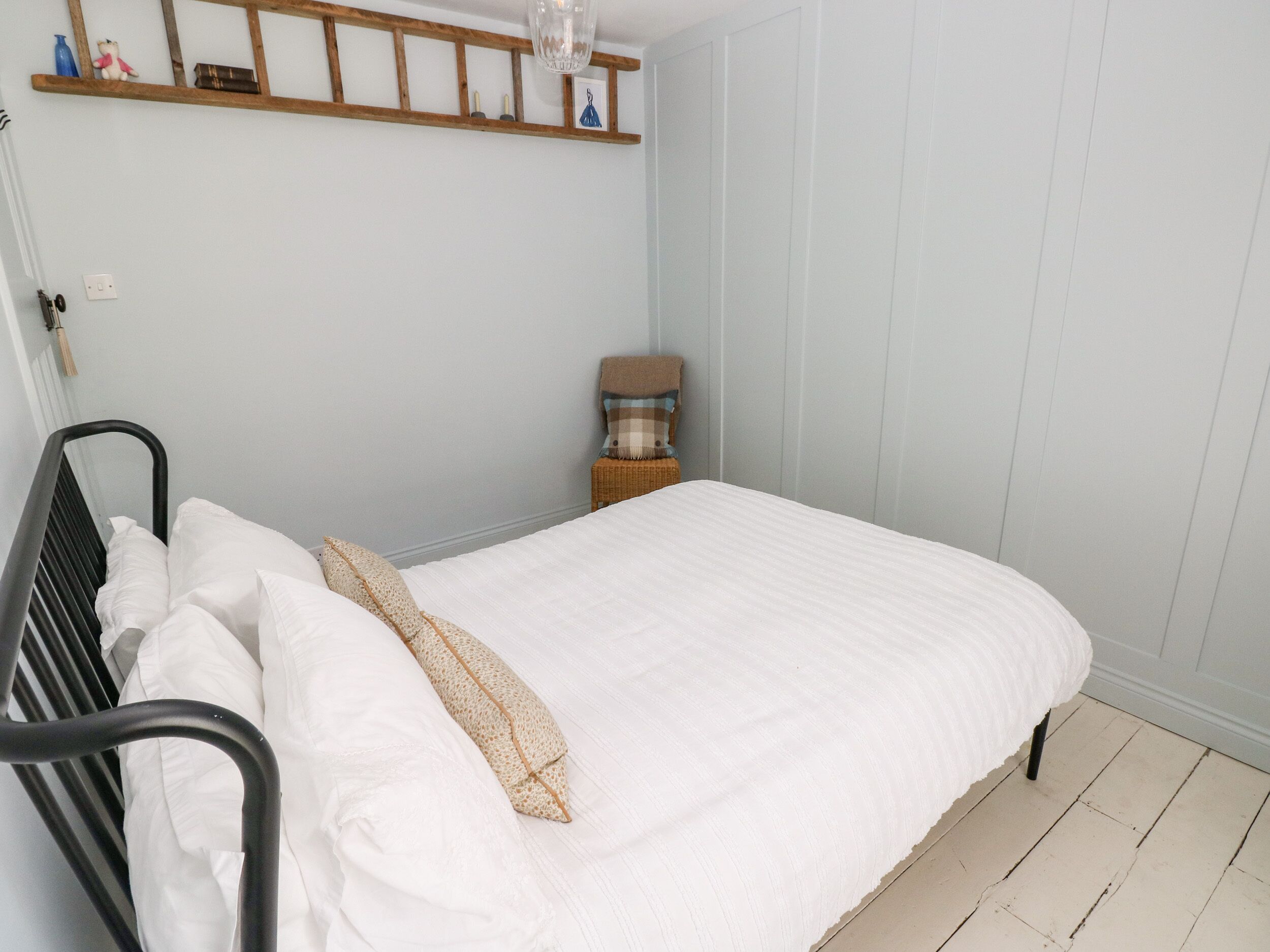A neatly made bed with white linens and a single decorative pillow. A wooden shelf above the bed holds a few small items.