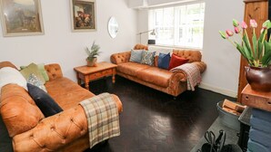 Een woonkamer met een bruine leren bank, een houten salontafel en een open haard.