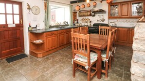 A kitchen with wooden cabinets, a dining table with chairs, a stove, and a sink. - Harbour Cottage (Watchet)