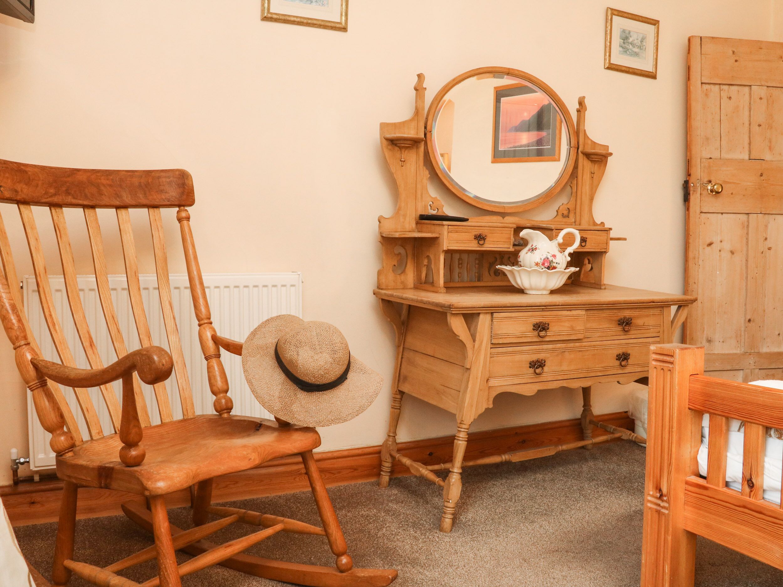 A wooden rocking chair, a wooden dresser with a mirror, and a small table with a pitcher.