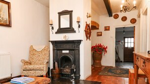 A cozy living room with a fireplace, a patterned armchair, a coffee table with books, and a large vase of red flowers. - Harbour Cottage (Watchet)