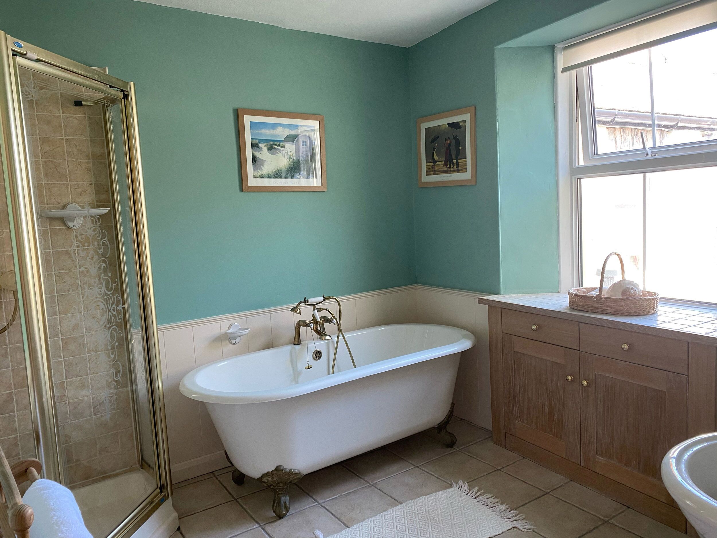 Une salle de bain avec une baignoire sur pieds, un espace douche, des meubles en bois et deux tableaux encadrés au mur.