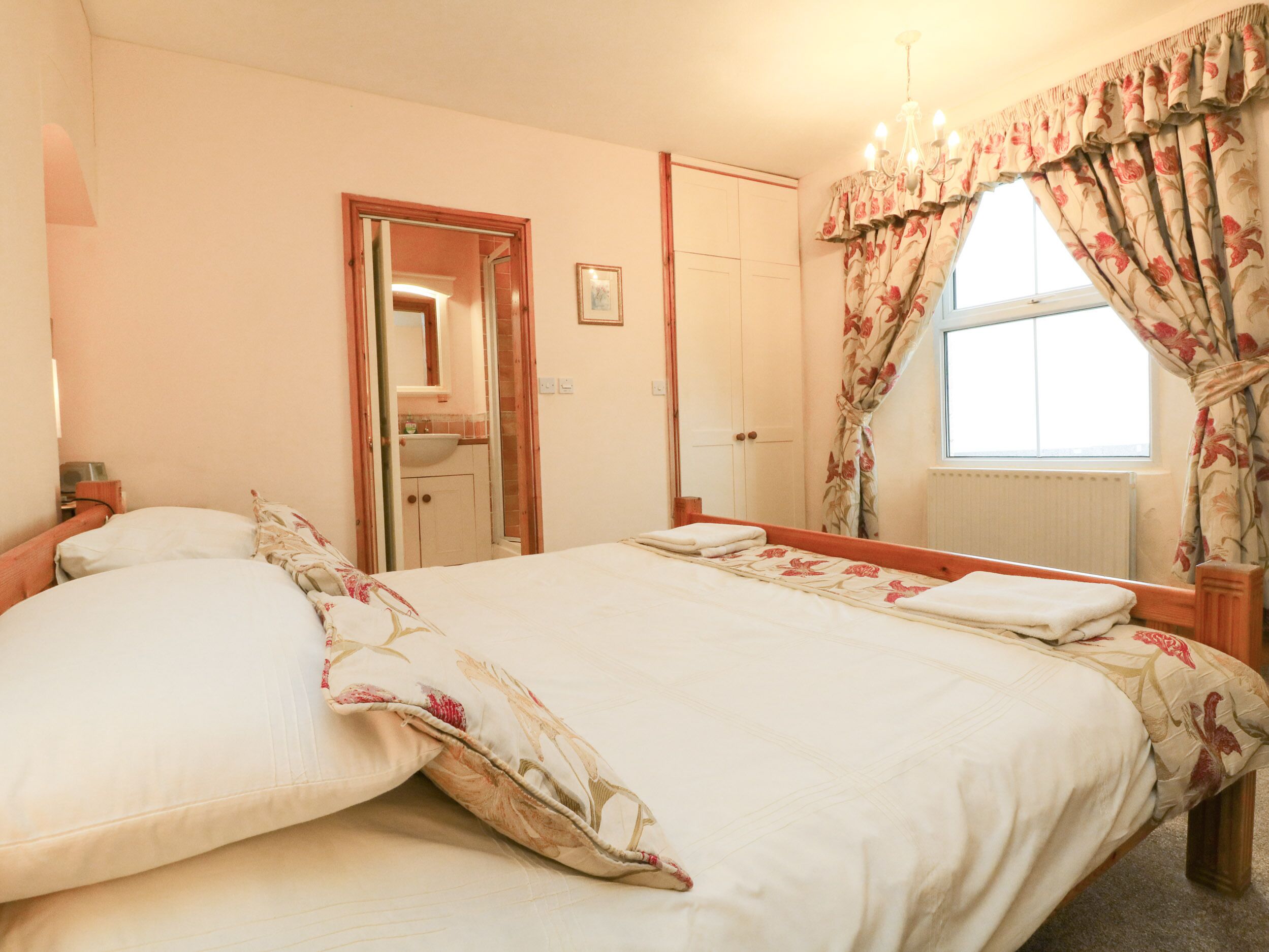 A bedroom with a large bed, a mirror, a window with floral curtains, and a door leading to a bathroom.