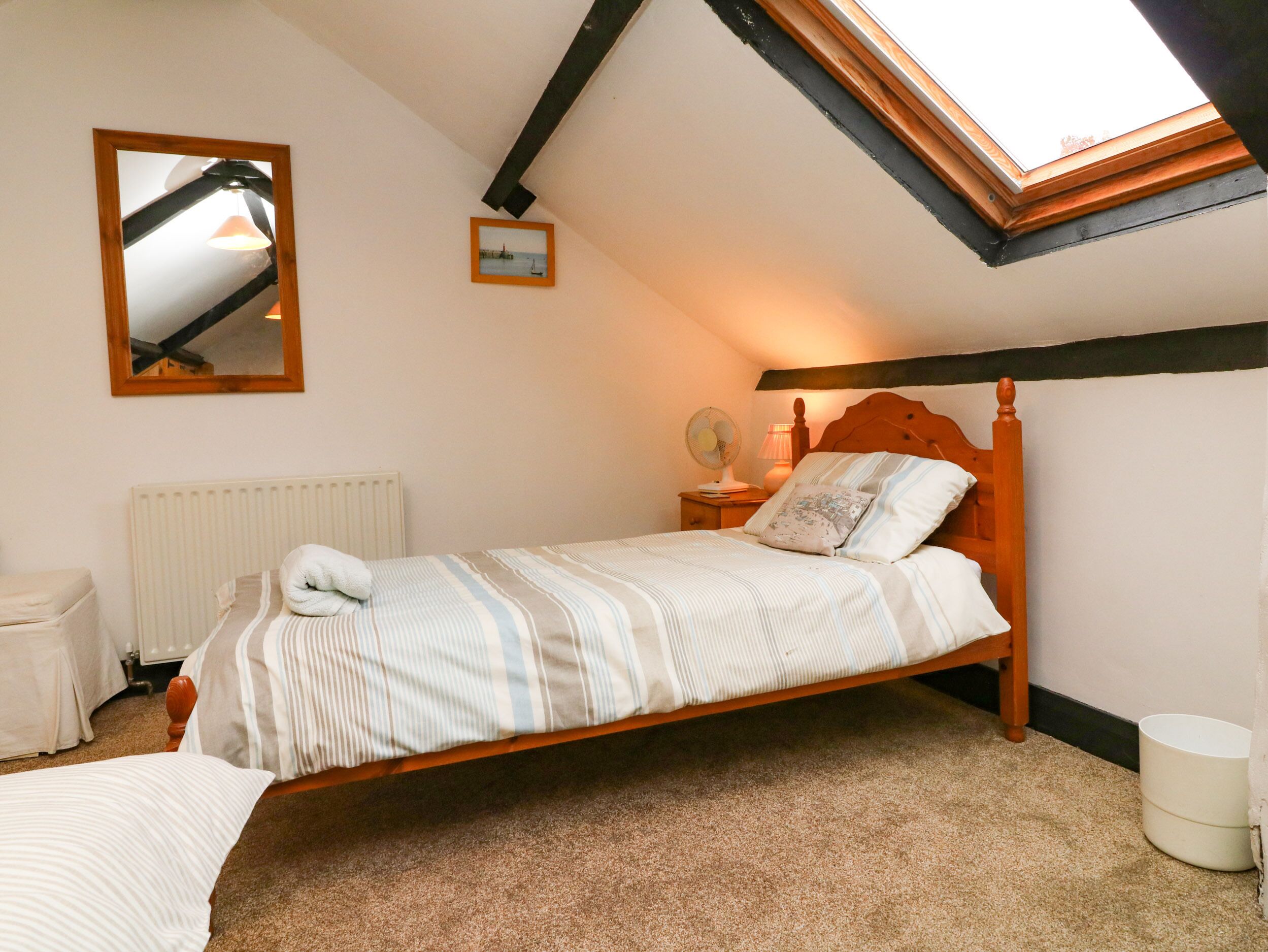 A bedroom with a sloped ceiling, a wooden bed, a radiator, a bedside table with a lamp, and a small picture frame.