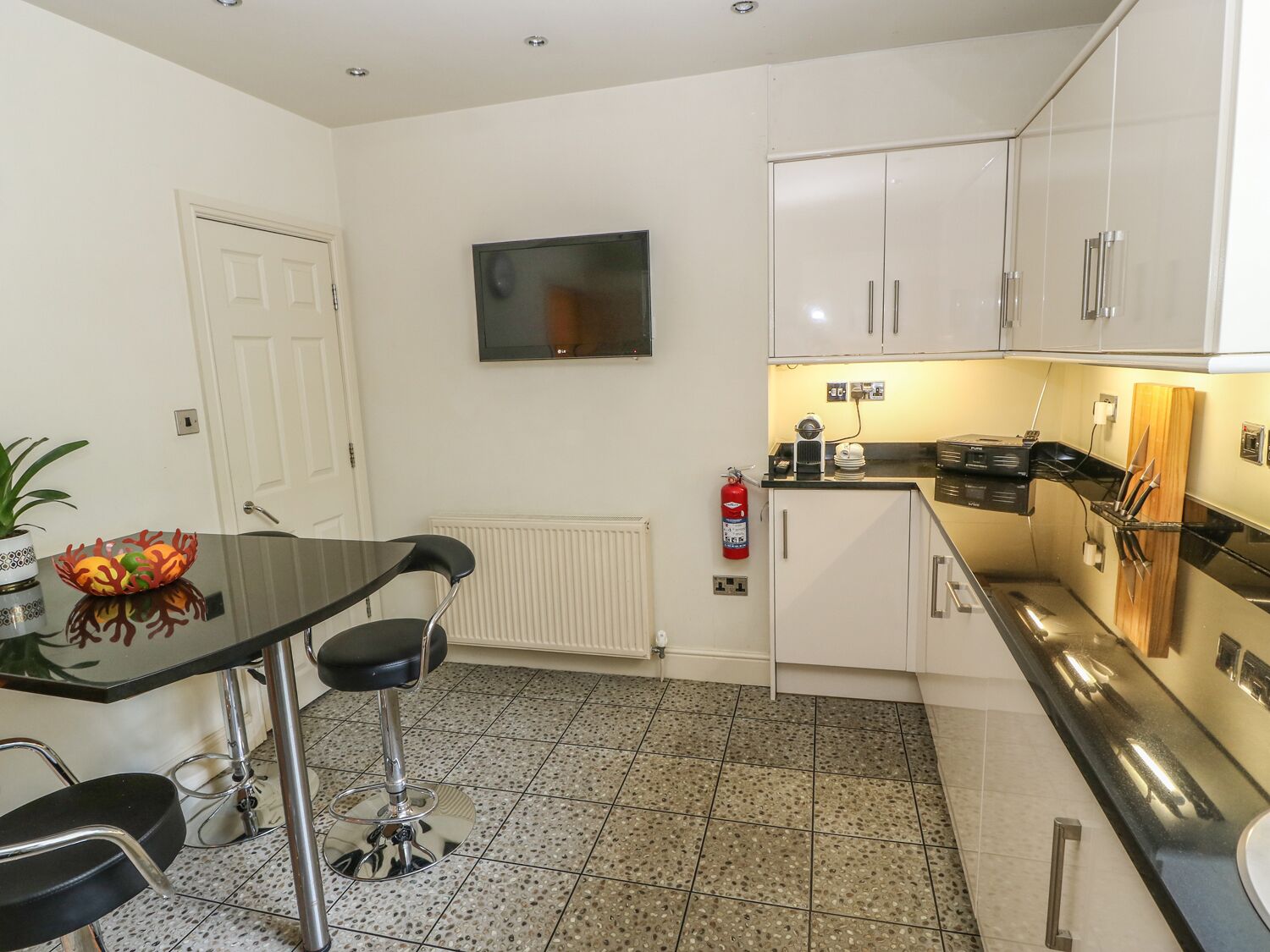 Uma cozinha compacta com área de jantar, armários brancos, bancada preta e piso de azulejos.