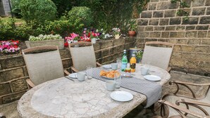 Un patio al aire libre con una mesa redonda, seis sillas de mimbre y una pared de piedra.