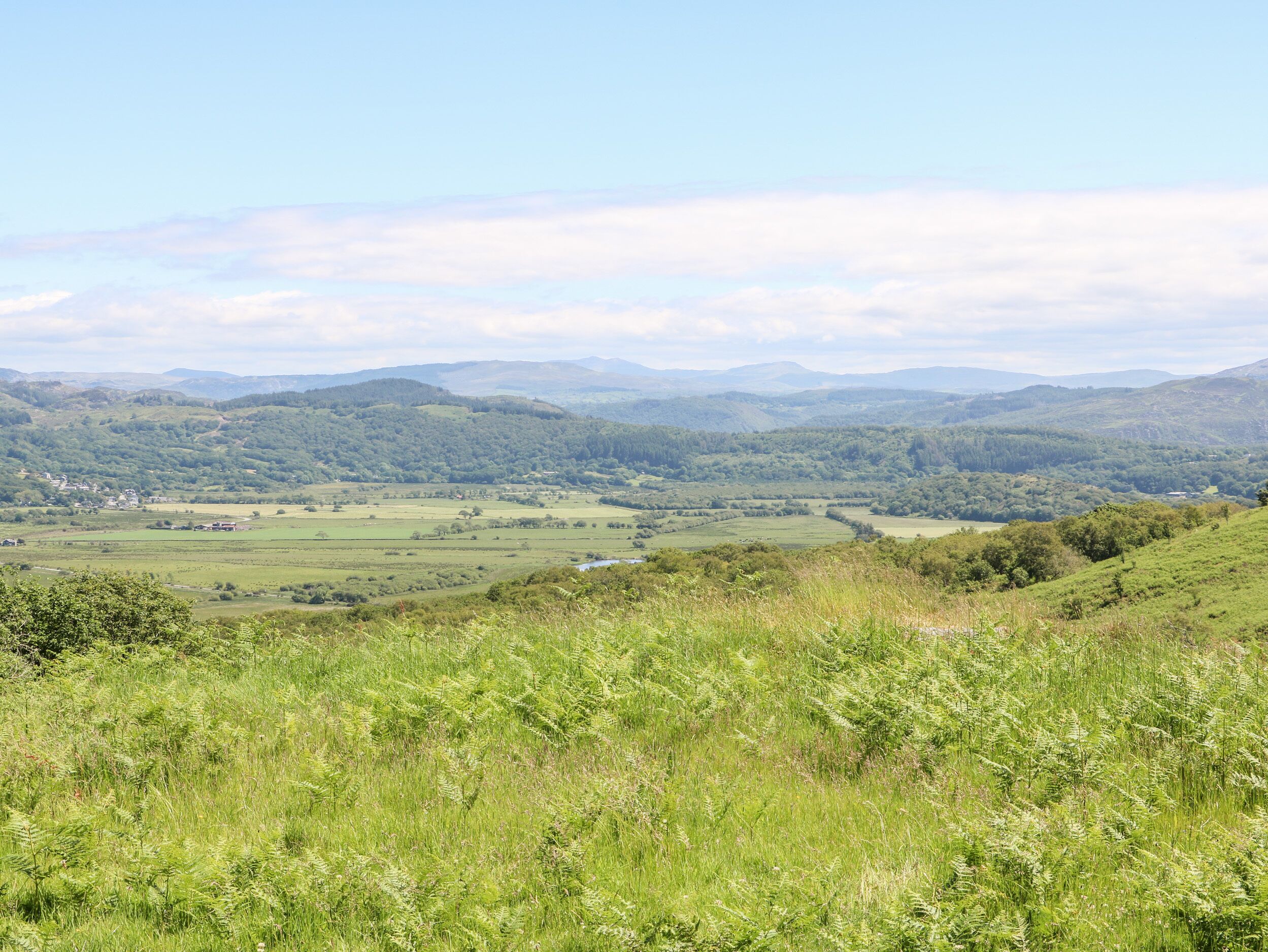 A panoramic view of a lush green valley with rolling hills and distant mountains under a clear sky.