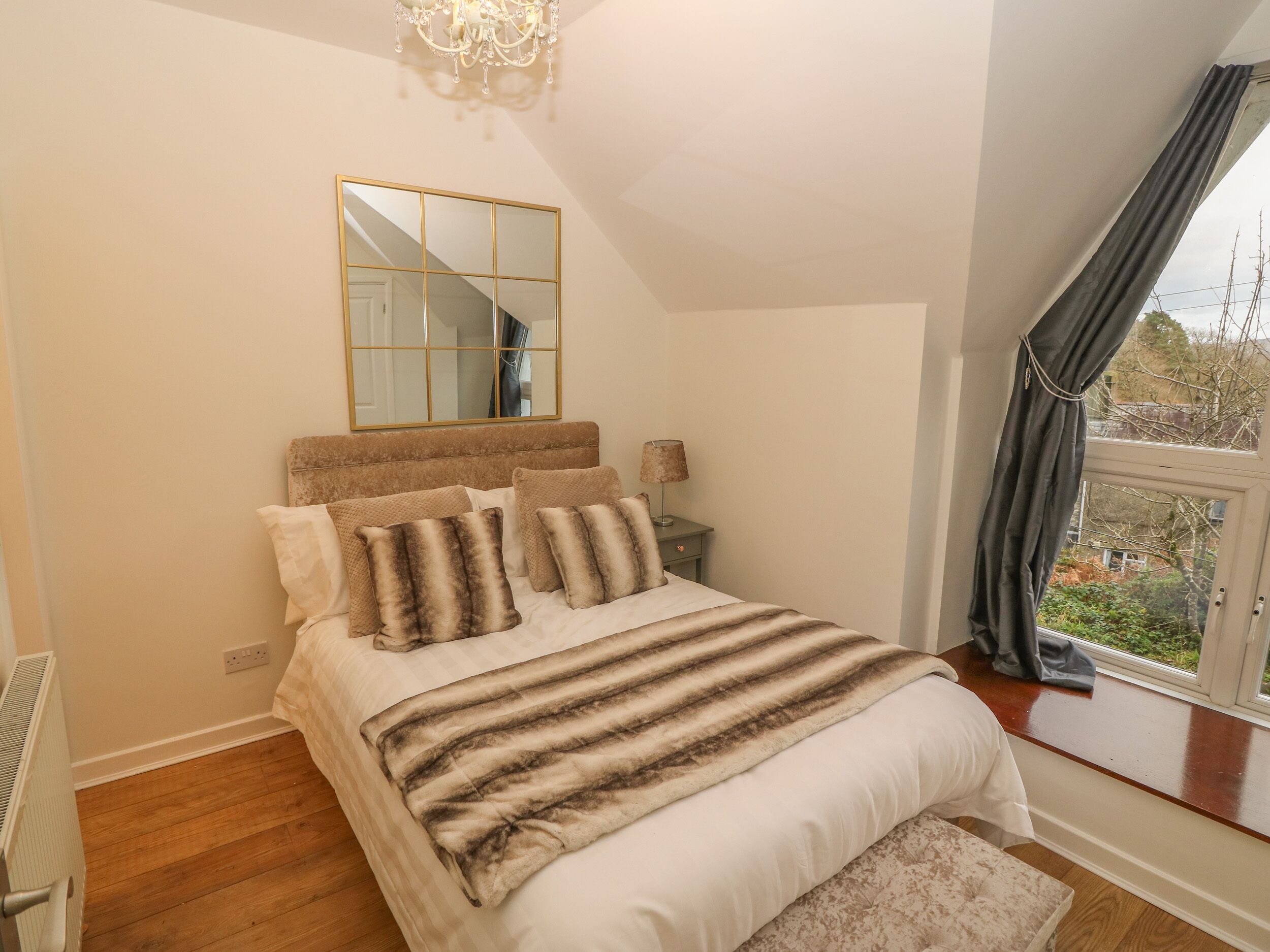 A bedroom with a large bed, a bedside table with a lamp, a mirror, and a window with curtains.