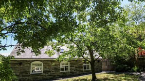 A stone house with a sloped roof and arched windows, surrounded by a gravel path and a grassy area. - Yr Hen Ysgol, The Old School (Porthmadog)