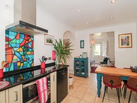 Uma cozinha com um mosaico colorido, uma área de refeições com mesa e cadeiras de madeira, e vista para a sala de jantar.