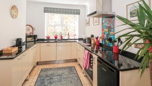 Une cuisine moderne avec des meubles de couleur claire, un plan de travail noir, une cuisinière encastrée et une grande fenêtre donnant sur un paysage verdoyant.