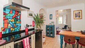 Une cuisine avec un mur de crédence aux couleurs vives, un coin repas avec une table et des chaises en bois, et une vue sur la salle à manger.