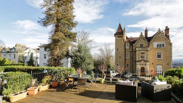 Une terrasse sur le toit, aménagée avec du mobilier d’extérieur, un grand arbre et, en arrière-plan, un bâtiment historique.