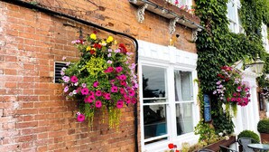 A brick building with a window and hanging flower baskets. - The Escape (Malvern)