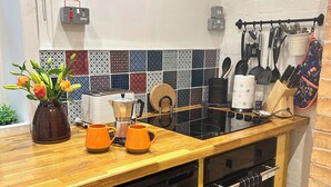 A modern kitchen with a wooden countertop, a coffee maker, two orange mugs, and a variety of utensils hanging on a rack. - The Escape (Malvern)