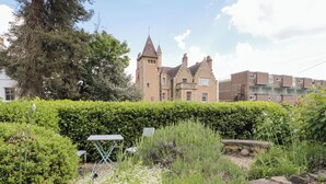 A historic building with a tower, surrounded by well-maintained hedges and a small garden area with a table and chairs. - The Escape (Malvern)
