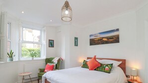 A bedroom with a large bed, a window with shutters, a radiator, a small table, and a green chair. - The Escape (Malvern)