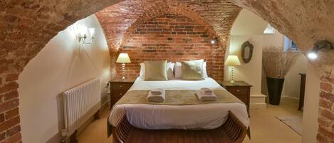 A cozy room with a brick wall, a wooden bench, a bed with white linens, and a potted plant.