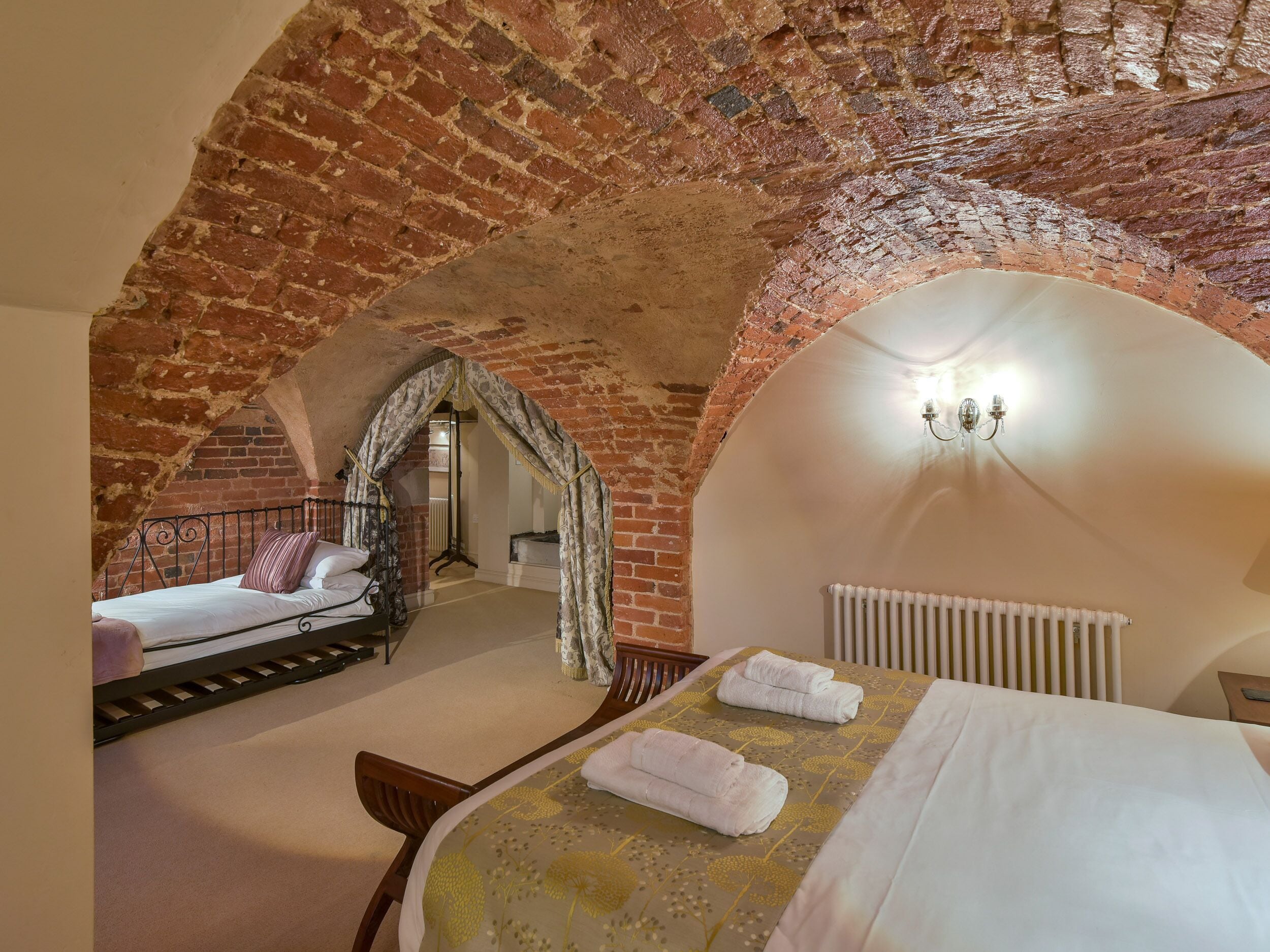 Ein Schlafzimmer mit Ziegeldecke, einem Bett mit weißen Leinen, einem Holzstuhl und einem Heizkörper.