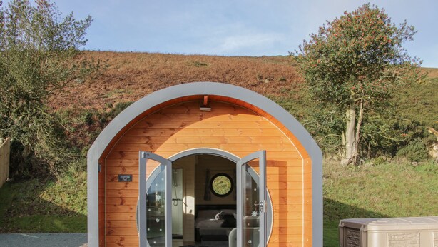 Une cabane en bois dotée d’une porte circulaire et dont on peut apercevoir l’espace douche à l’intérieur.