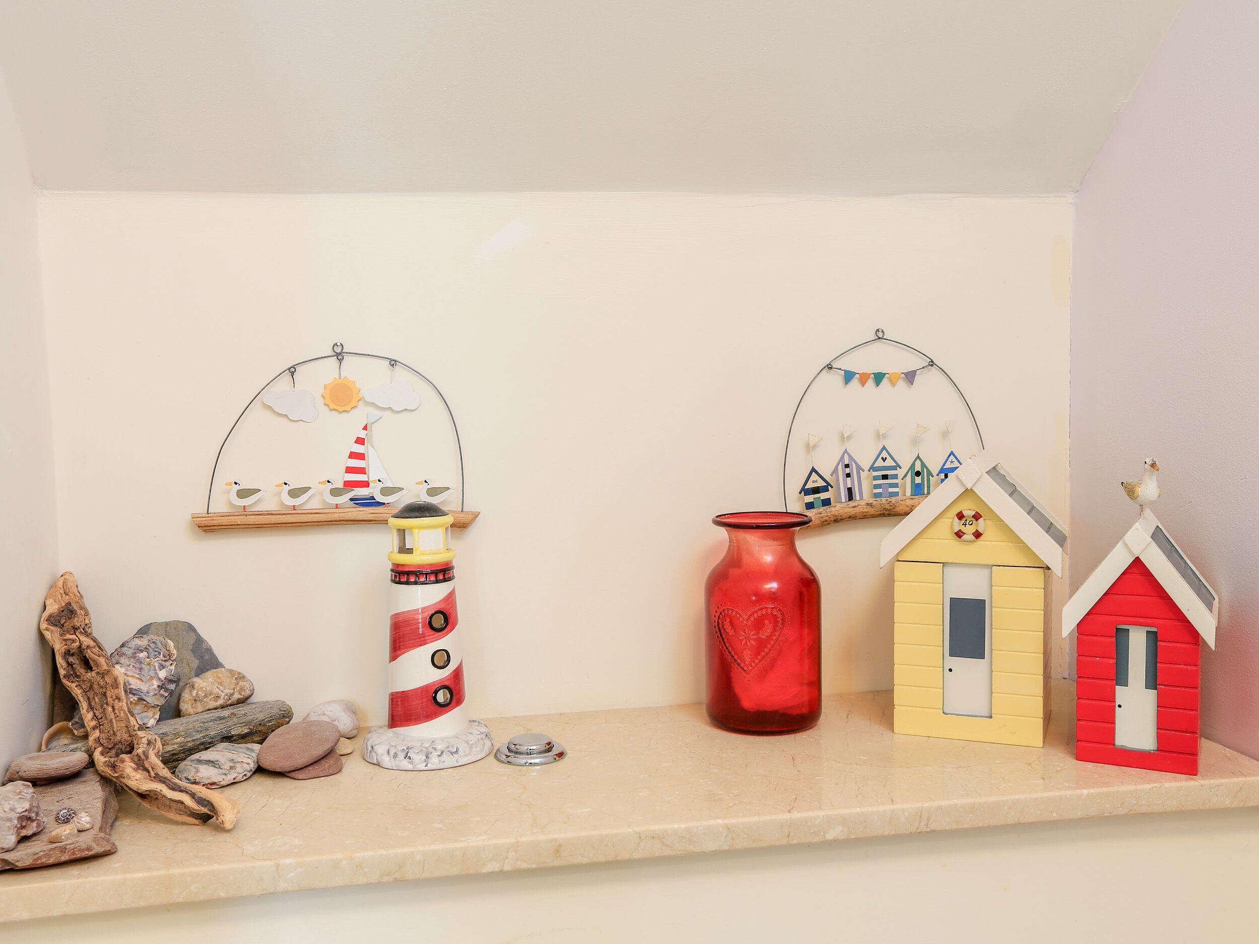 A shelf with a lighthouse, a red vase, and two small houses.