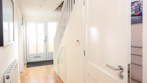 A hallway with a white door, a radiator, and a staircase with white railings. - 2 The Bay (Kingsbridge)