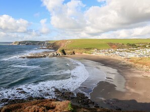 A coastal scene with a sandy beach, rocky shoreline, and a village in the background. - 2 The Bay (Kingsbridge)