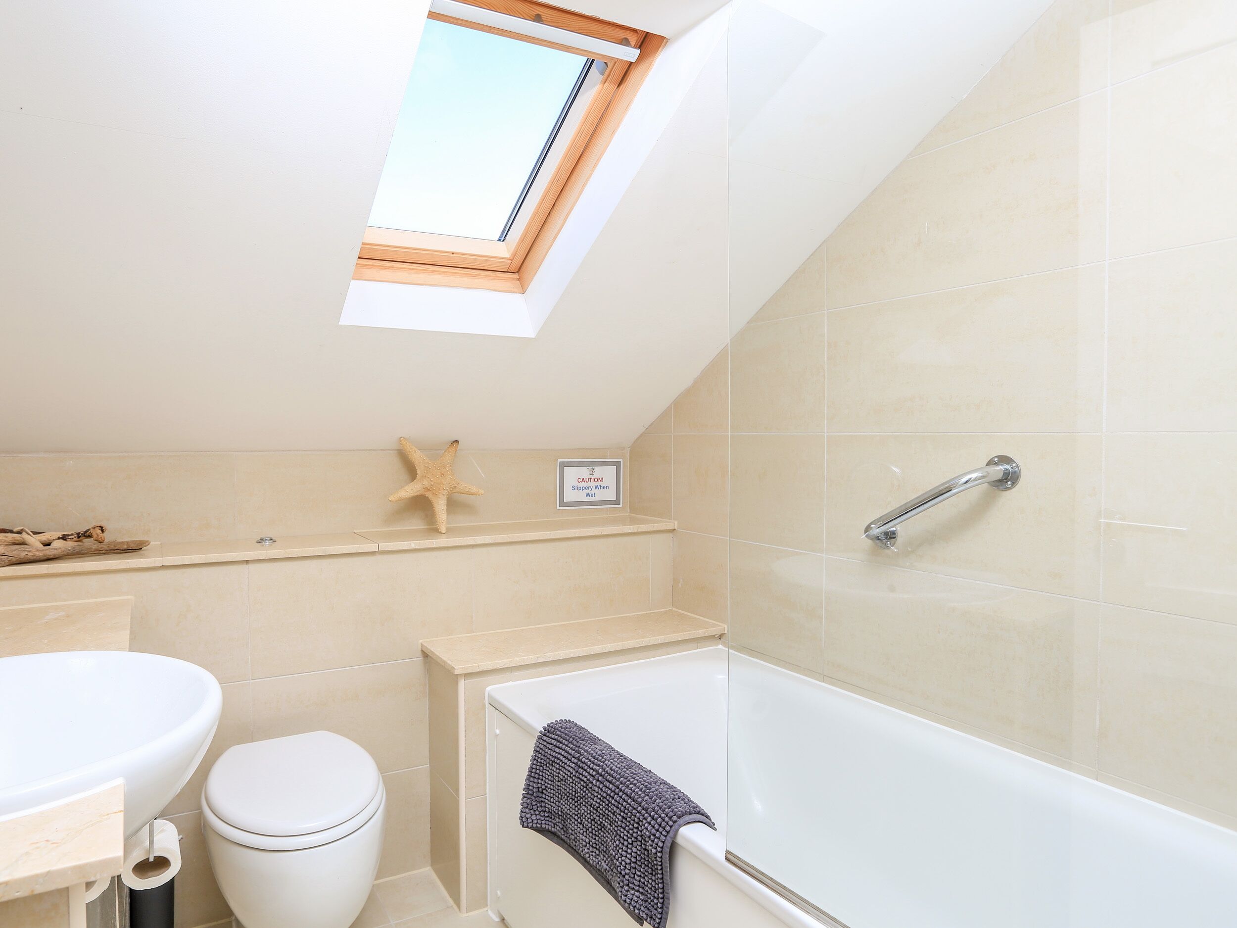 A bathroom with a skylight, a bathtub, a toilet, and a starfish decoration.
