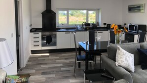 A modern kitchen with a black range hood, white cabinets, and a window overlooking a garden. - 1 Barn Cottages (Whitchurch)