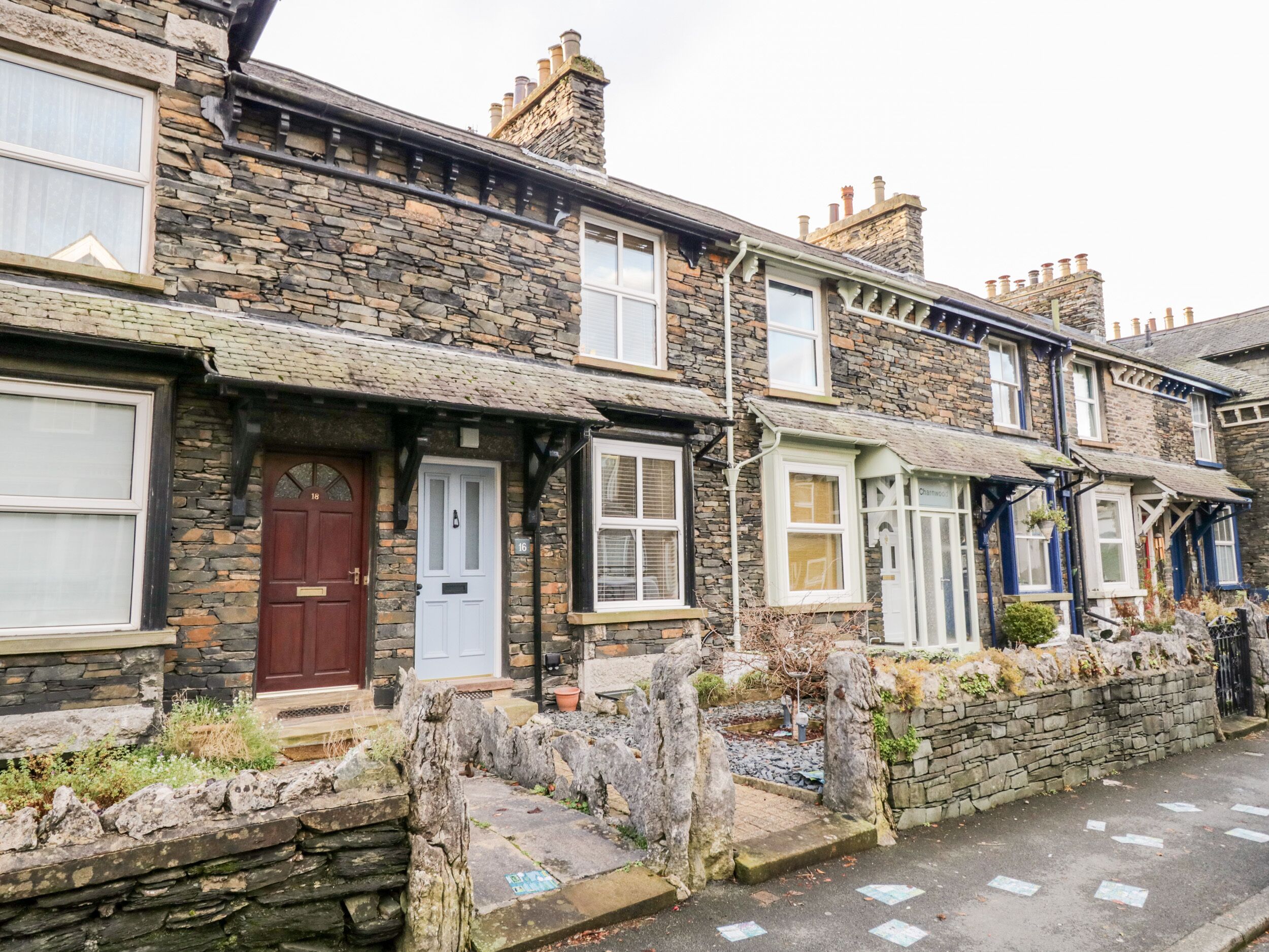 A row of traditional stone houses with distinct front doors and windows, a stone wall, and a paved street.