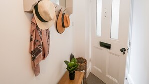 A hallway with a coat rack holding hats and a jacket, a potted plant on a small table, and a door with a keyhole. - Pottergill (Windermere)