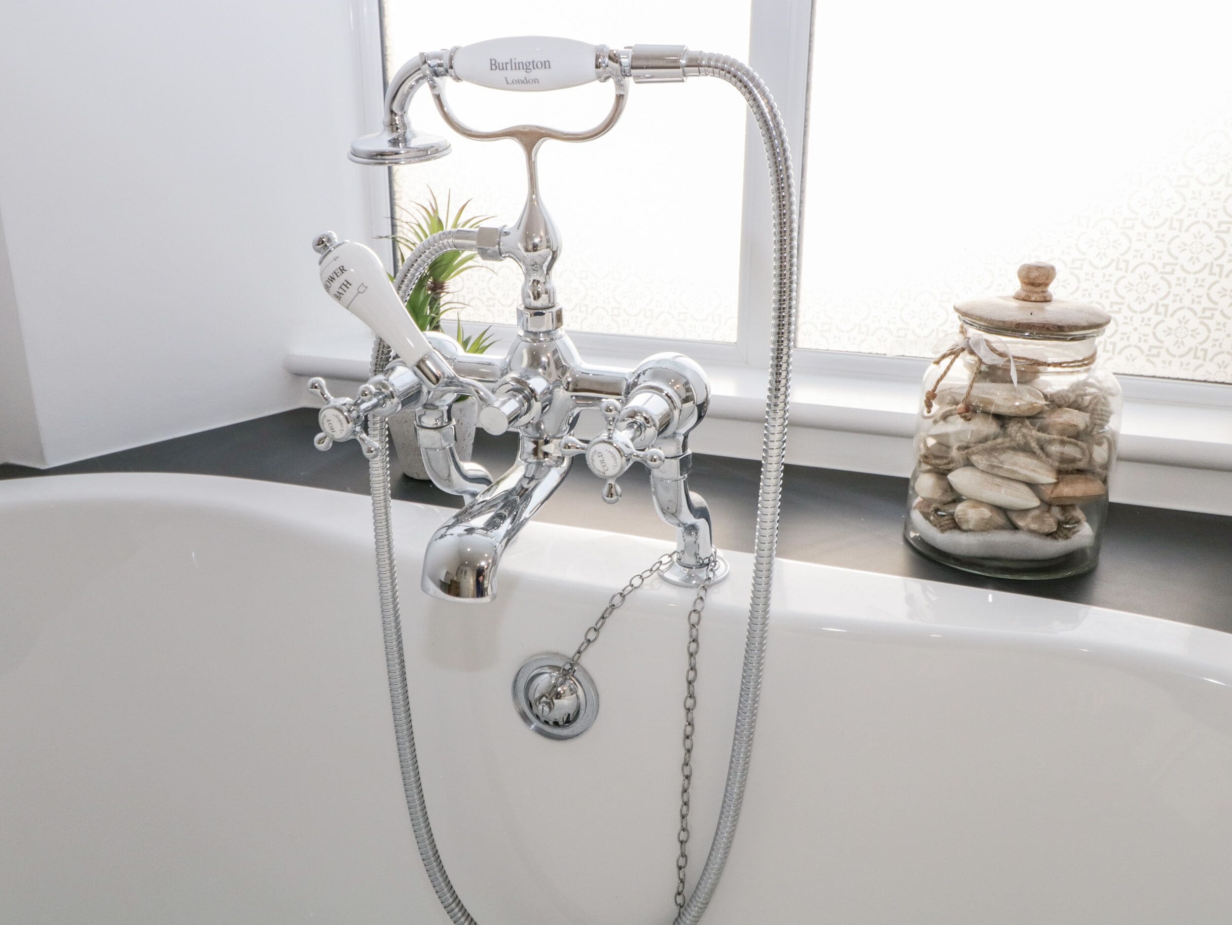 A bathroom with a bathtub, a shower, and a glass jar with seashells on the counter.