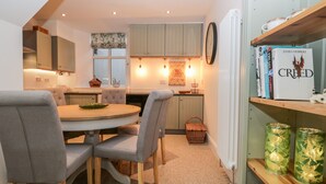 A compact kitchen with a dining area, featuring a round table, grey upholstered chairs, and wooden flooring. - Pottergill (Windermere)