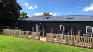 A two-story house with a dark exterior, a metal roof, and a wooden fence. - 2 Barn Cottages (Whitchurch)