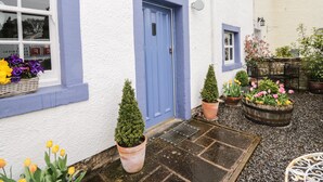 Un edificio bianco con una porta e delle finestre azzurre, circondato da vasi con piante e fiori.