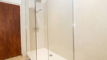 A modern bathroom with a glass-enclosed shower, a wooden door, and a marble floor.