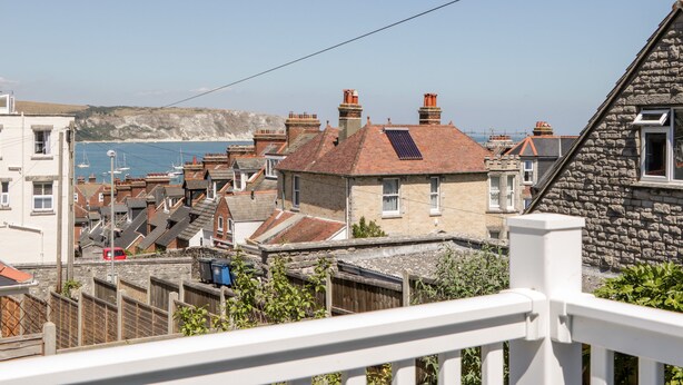 A coastal residential area with stone and brick houses, a visible sea, and a clear sky. - Seaview (Swanage)
