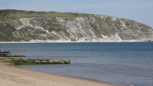 A coastal landscape with a sandy beach, calm sea, and a large cliff with layered rock formations. - Seaview (Swanage)