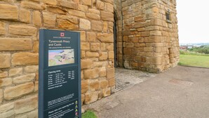 Un edificio de piedra con un cartel que detalla el Priorato y el Castillo de Tyemouth, incluyendo horarios de apertura y precios de entrada.
