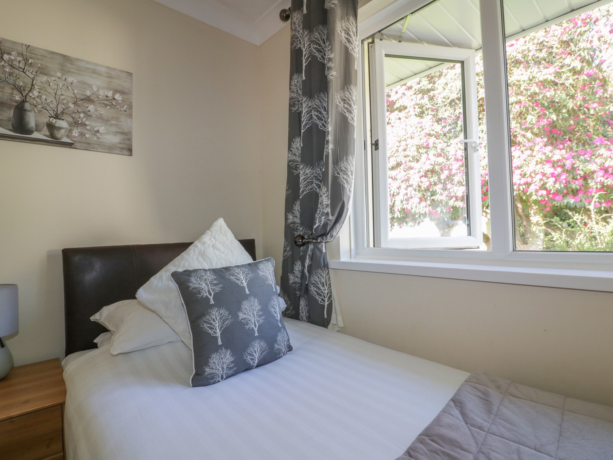 A bedroom with a bed, a nightstand, a lamp, a window with curtains, and a painting on the wall.
