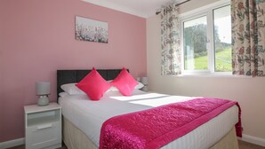 Une chambre à coucher avec un lit, une table de chevet, une lampe, une fenêtre avec des rideaux et un tableau au mur.