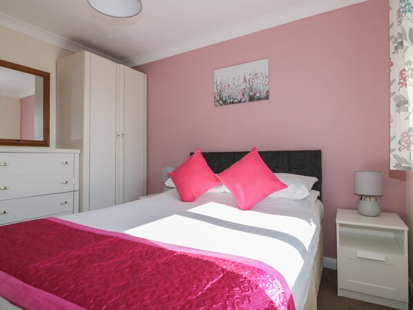 Une chambre à coucher comprenant un lit, une table de chevet, une commode, un miroir et un tableau représentant des motifs floraux accroché au mur.