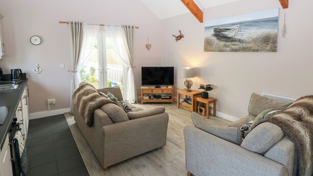 A cozy living room with two sofas, a TV, and a painting of a boat on the wall. - Love Cottage (Tenby)