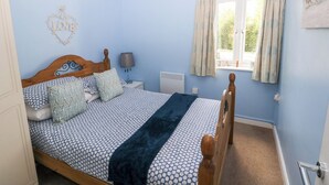 A bedroom with a wooden bed, a chandelier, a window with curtains, and a wall decoration. - Love Cottage (Tenby)